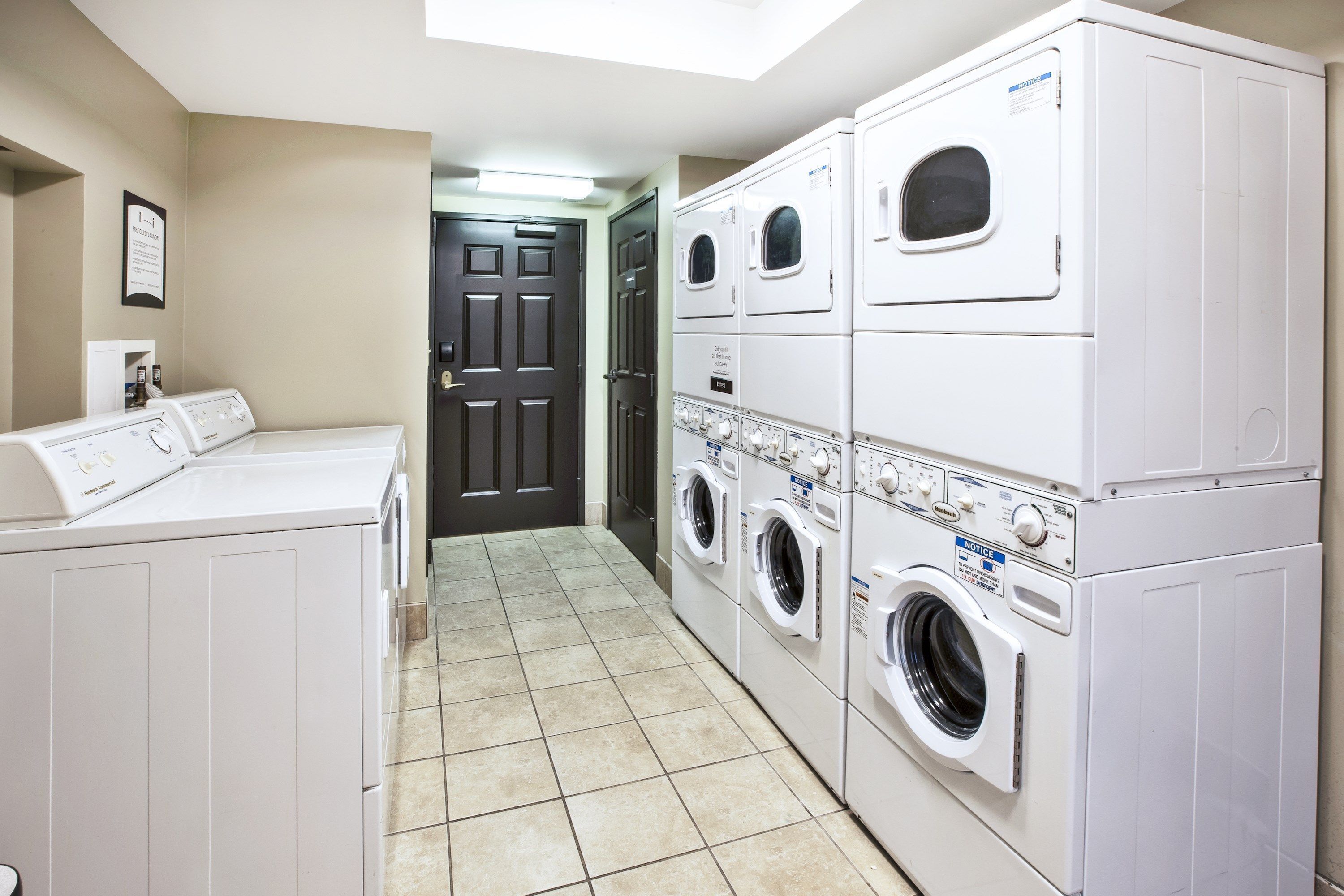 A laundry room with multiple stacked washers and dryers, a door, and a tiled floor.