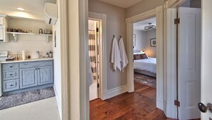 Un pasillo que conduce a un dormitorio con cama, un baño con ducha y una cocina con armarios y encimera.