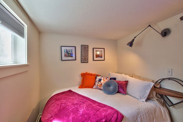 A bedroom with a bed, pillows, a blanket, a wall-mounted lamp, and framed pictures on the wall. - HISTORICAL VICTORIAN, BEAUTIFULLY RESTORED (McMinnville)