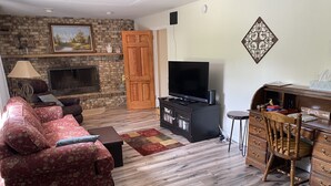 A living room with a fireplace, a television, a desk with drawers, and a red sofa. - Our Comfortable Neighborhood Home (Boalsburg)