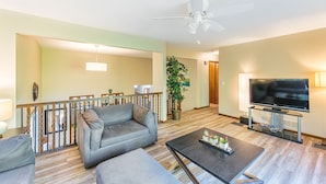 Ein Wohnzimmer mit grauem Sofa, einem Couchtisch, einem Fernseher auf einem Schrank, einem Deckenventilator und einer Treppe, die in einen anderen Raum führt.