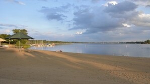 Ein Strand mit einem grünen Sonnenschirm, Booten und einem ruhigen See.