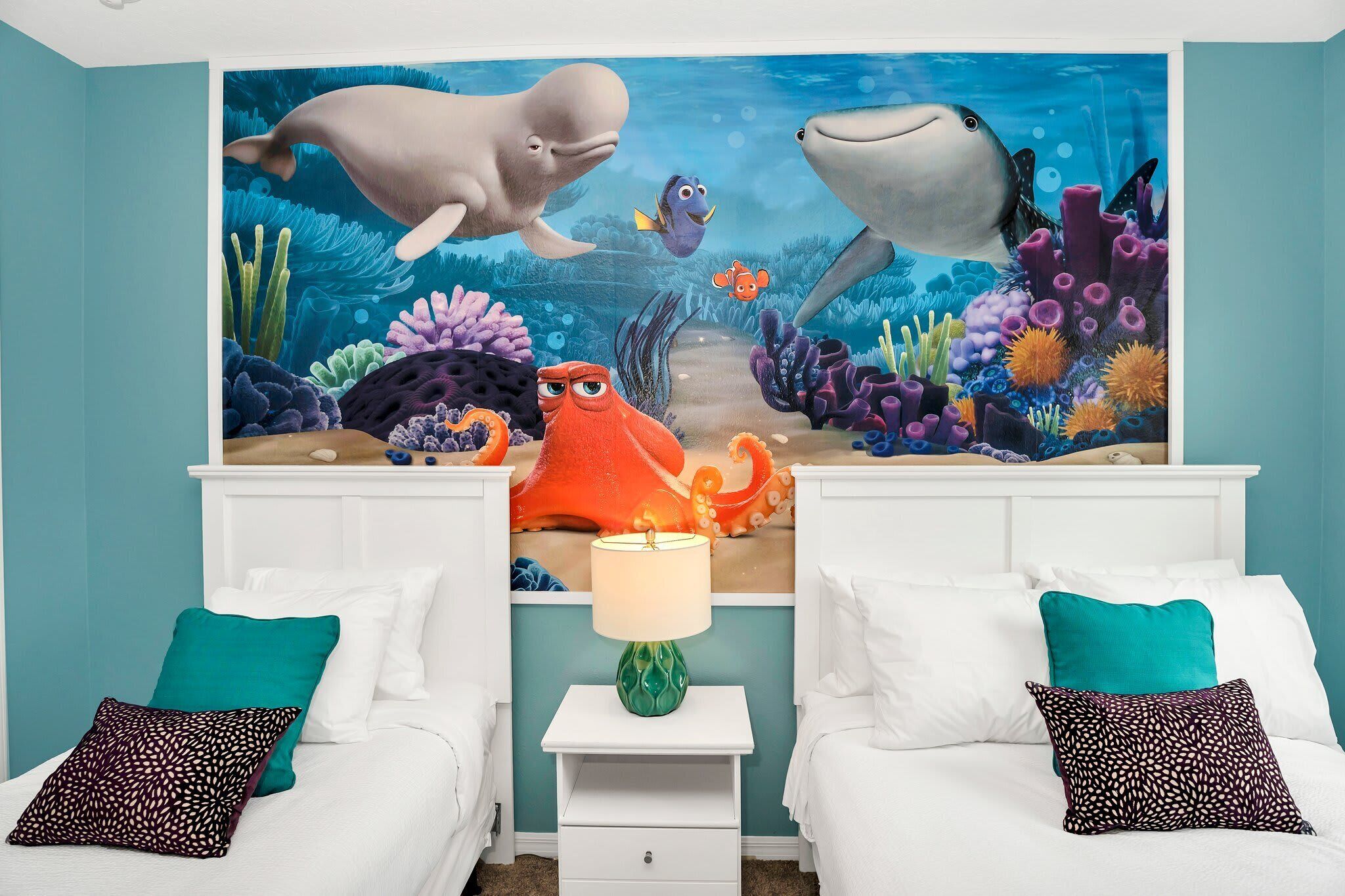 A bedroom with two beds, a nightstand, and a wall mural of an underwater scene.