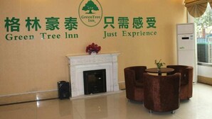 Rezeptionsbereich eines Green Tree Inn mit Kamin, Sitzgelegenheiten und einer Wand mit dem Hotel-Logo und -name.