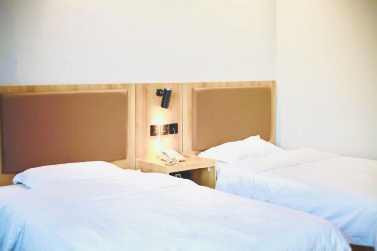 Habitación de hotel con dos camas individuales, un cabecero de madera, una mesita de noche con lámpara y teléfono.