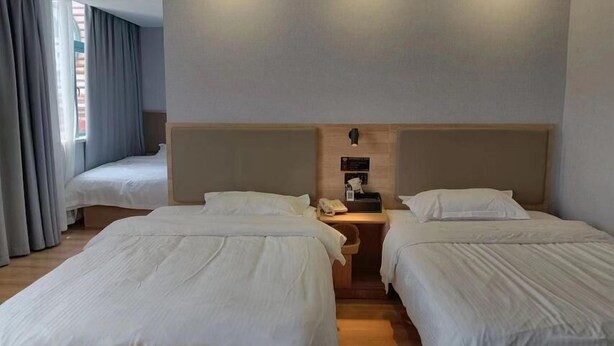 Ein Hotelzimmer mit zwei Einzelbetten, einem kleinen Schreibtisch mit Lampe und einem Fenster mit Vorhängen.