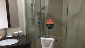 Um banheiro com chuveiro em gabinete de vidro, pia com bancada escura e toalha em um porta-toalhas.