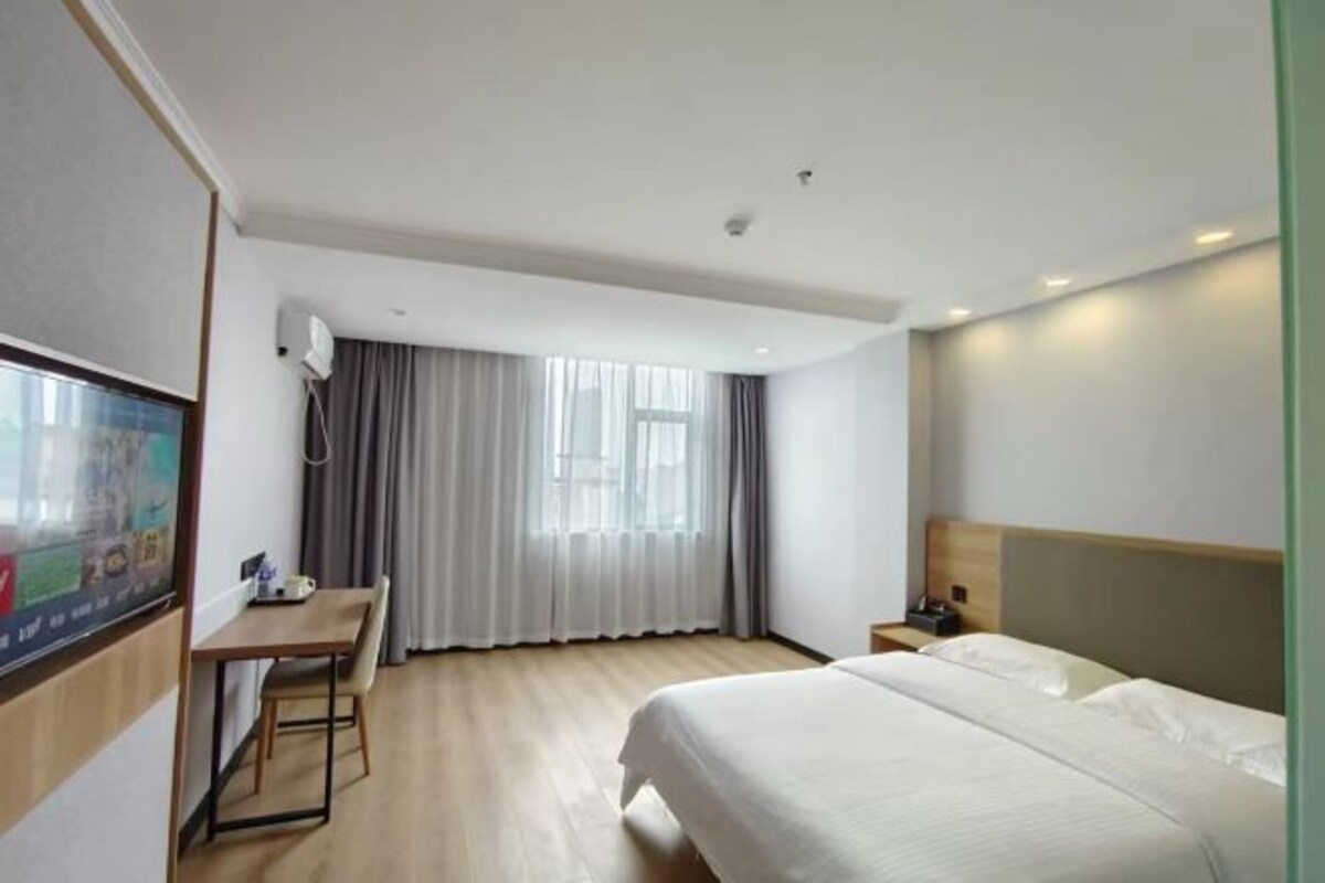 Una habitación de hotel con cama, escritorio, televisor y ventana con cortinas.