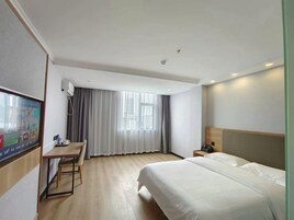 Una habitación de hotel con cama, escritorio, silla, televisor y ventana con cortinas.