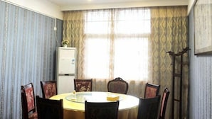 Uma sala de conferências com uma mesa redonda, cadeiras, uma luminária no teto e cortinas estampadas.