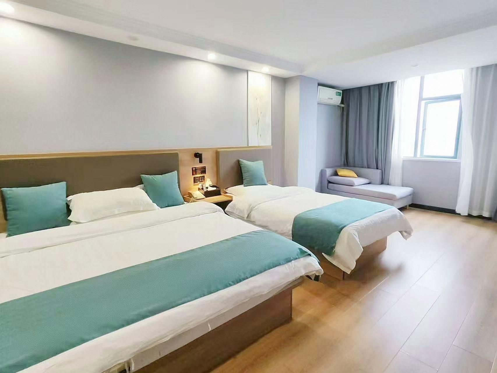 A hotel room with two beds, a sofa, a bedside table with a lamp, and a window with curtains.