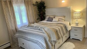 Une chambre à coucher avec un lit, une table de chevet, une lampe et une grande fenêtre avec des rideaux.