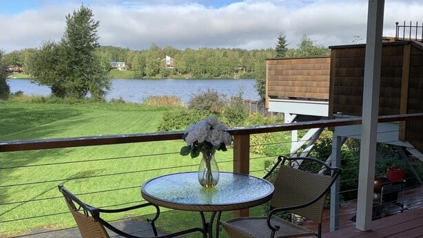 Une terrasse avec une table ronde et deux chaises, offrant une vue sur un lac et une forêt.