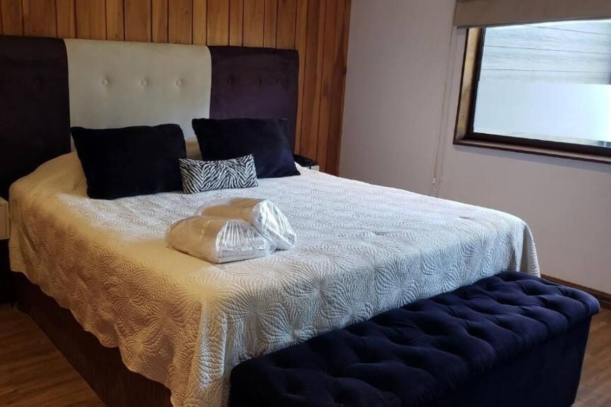 A bedroom with a bed, a nightstand, a window, and a wooden headboard.