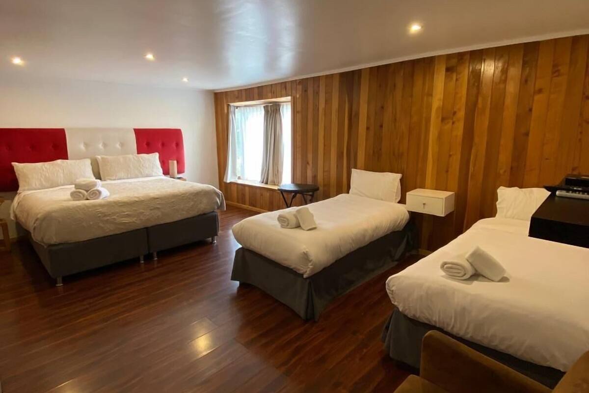 A hotel room with two beds, a wooden paneled wall, and a window with curtains.
