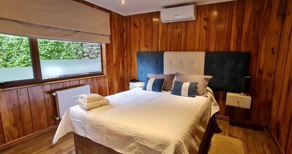 Un dormitorio con paneles de madera, una cama, mesitas de noche y un ventanal.