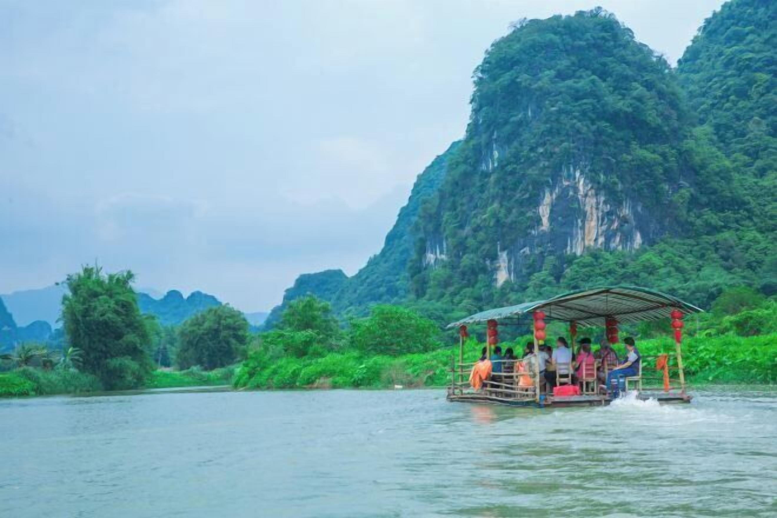 A riverboat with passengers, surrounded by lush greenery and mountains.