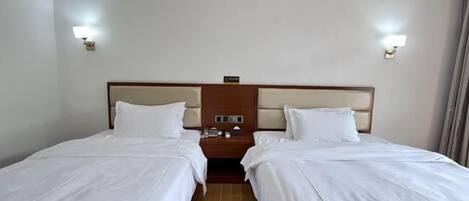 Quarto de hotel com duas camas de solteiro, cabeceira de madeira, mesas de cabeceira com luminárias e uma pequena mesinha de apoio.