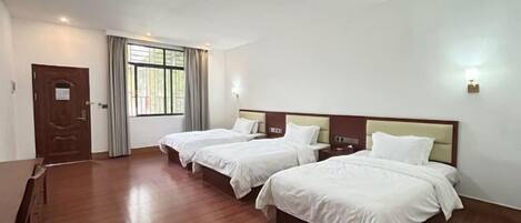 A hotel room with three beds, a wooden floor, a door, and a window with curtains.