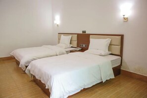 A hotel room with two beds, each with white bedding and headboards. There are wall-mounted light fixtures on either side of the beds.