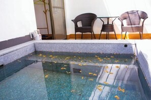A clear pool with floating leaves, surrounded by wicker chairs and a table, with a glass door and a plant in the background. - Yingxi Tangquan Resort (Yingde)