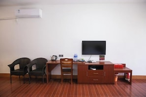 A room with a wooden desk, two chairs, a television, and an air conditioning unit.