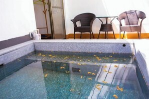 A clear pool with a stone edge, two wicker chairs, and a small table.
