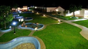 Un espace paysager agrémenté de plusieurs éléments d’eau de forme circulaire et d’une piscine centrale au motif décoratif, le tout entouré de pelouses bien entretenues et de sentiers.