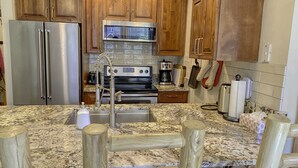 A kitchen with wooden cabinets, stainless steel appliances, a granite countertop, and a wooden stool. - Fernie ON THE MOUNTAIN luxury 2 bedrooms 3 beds (1 king, 2 queen), 2 baths.  (Fernie)