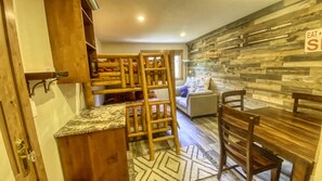 Una stanza accogliente con un letto a castello, un tavolo da pranzo con sedie, un divano e un pannello di legno con un cartello.