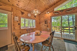 A wooden cabin interior with a round dining table, chairs, a chandelier, and large windows offering a view of the outdoors. - Atlanta Waterfront Cabin w/ Dock & Kayaks! (Atlanta)