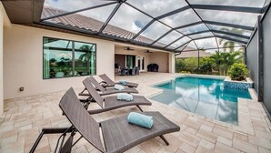 A covered outdoor area with a pool, lounge chairs, and a patio.
