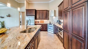A kitchen with dark wood cabinets, a granite countertop, stainless steel appliances, and pendant lighting.