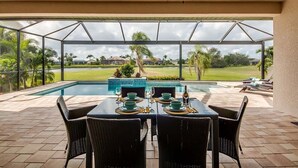 A covered outdoor dining area with a view of a swimming pool and a golf course.