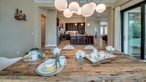 A dining area with a wooden table set for breakfast, a kitchen in the background, and pendant lighting.