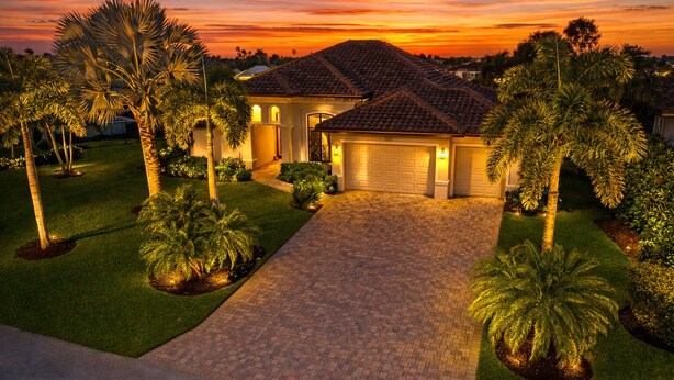 A residential property with a paved driveway, a garage, and well-maintained landscaping including palm trees and shrubs.