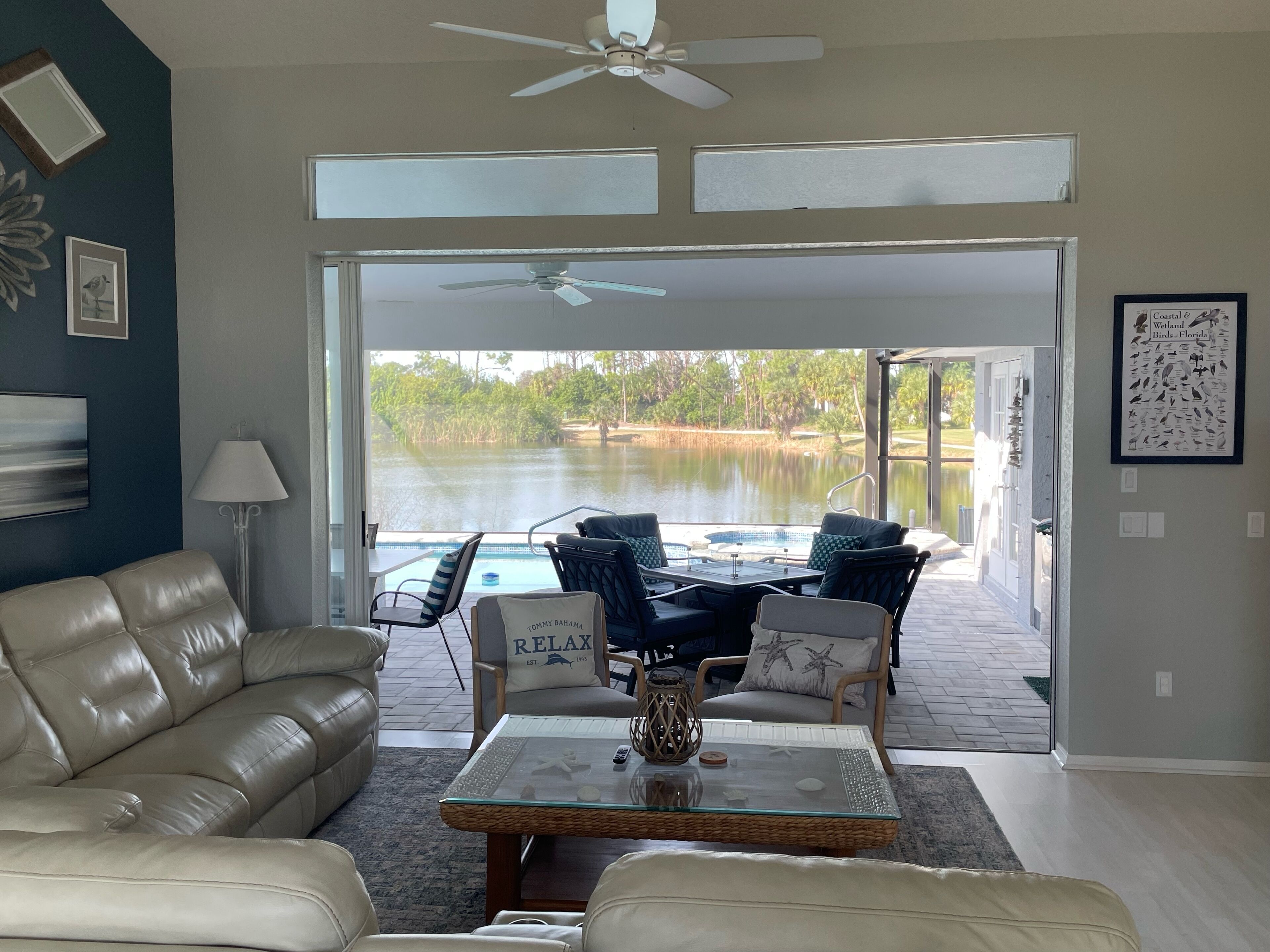 Un salon avec vue sur un lac, un ventilateur de plafond et un espace aménagé près de la piscine, avec des chaises et une table.