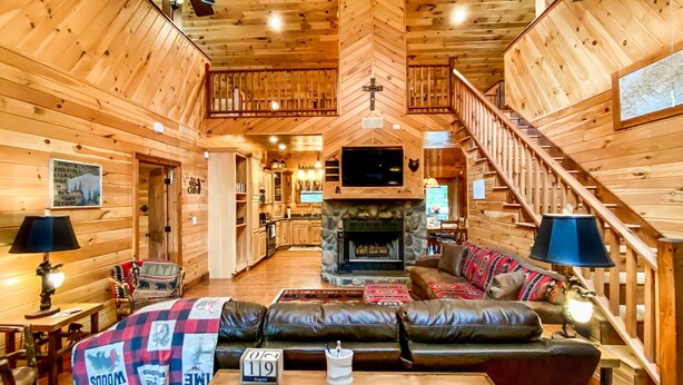 A cozy log cabin interior with a fireplace, leather sofa, wooden dining table, and a staircase. - Luxury Cabin in the Woods  (Franklin)