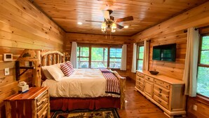 A wooden cabin bedroom with a bed, dresser, TV, and a view of the outdoors. - Luxury Cabin in the Woods  (Franklin)