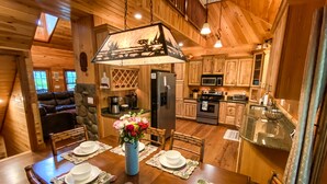 A wooden cabin interior with a dining table set for four, a refrigerator, microwave, stove, and a sink. - Luxury Cabin in the Woods  (Franklin)