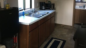 A compact kitchen with wooden cabinets, a built-in sink, and a coffee maker. - Lake Erie Lily Cabin (Fredonia)