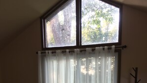 A room with a large window, a bed, a small table, and a coat rack. - Lake Erie Lily Cabin (Fredonia)