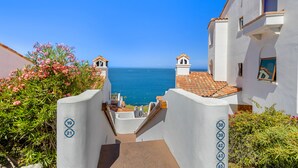 Un sendero costero que lleva a un edificio blanco con puertas numeradas, con vista al mar.