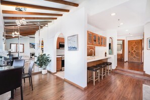 Una cocina moderna con armarios de madera, un comedor con mesa de vidrio y una escalera que sube a otro nivel.