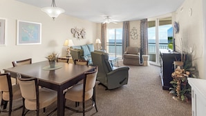 A spacious living area with a dining table, comfortable seating, a ceiling fan, and a view of the ocean through large windows. - 14TH FLOOR OCEANVIEW CONDO|SHORT WALK TO THE BEACH UNIT 1408|ACCESS TO AMMENTIES (North Myrtle Beach)