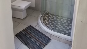 Ett badrum med en dusch som är avskärmad med glasväggar, en toalett och ett schackrutigt golv.