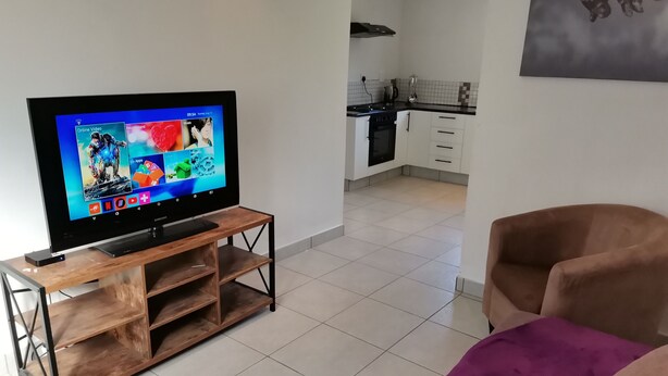 Ett vardagsrum med en tv-apparat på ett träbord, en lila soffa och ett kök i bakgrunden.