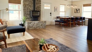 A spacious living room with a stone fireplace, a dining area with wooden furniture, and a ceiling fan. - New Raven Ranch-Dreamy Compound With Spa, Hammock Circle, Yoga Platforms, & More (Yucca Valley)