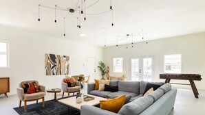 A spacious living room with a grey sofa, armchairs, a coffee table, and a foosball table. - New Raven Ranch-Dreamy Compound With Spa, Hammock Circle, Yoga Platforms, & More (Yucca Valley)