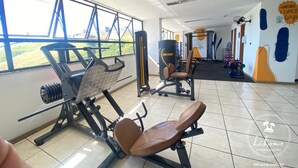 Un gimnasio con equipo de ejercicio, ventanas amplias y vista a espacios verdes.